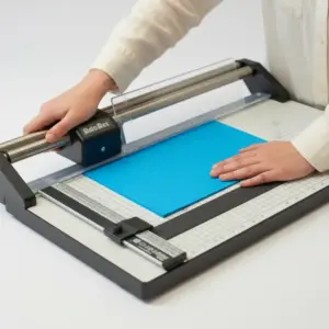 Person trimming a sheet of blue paper using a manual paper cutter